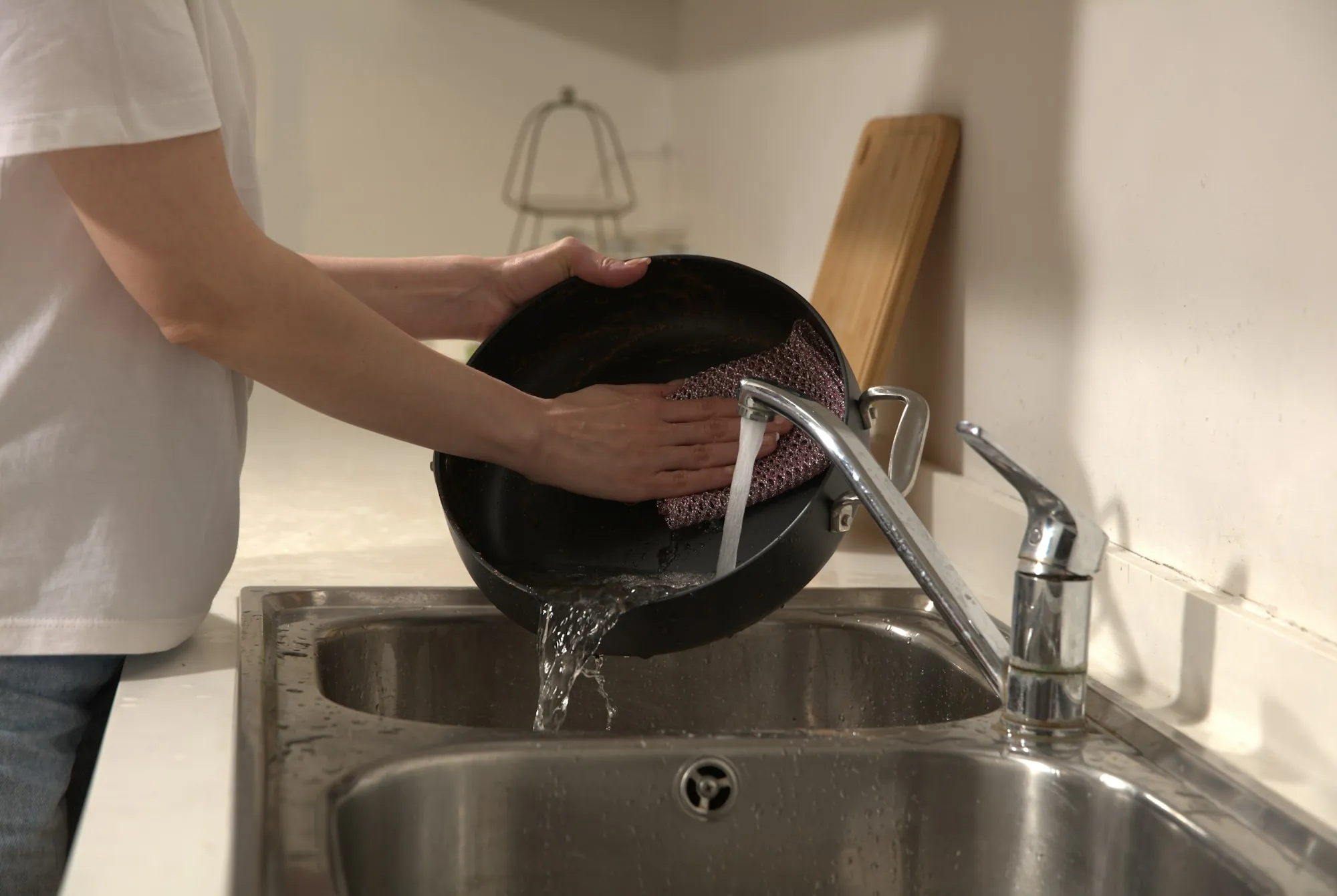 Person rinsing a pan under the faucet of a stainless steel kitchen sink